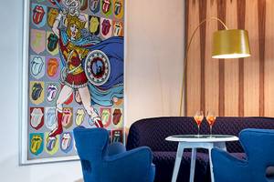 Innenbereich des Myconian Ambassador Hotels mit einem Sofa, einem Tisch und einer Wand mit Rolling Stones Kunstwerk.